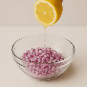 Suco de limão sendo espremido sobre cebola roxa picada em tigela de vidro.
